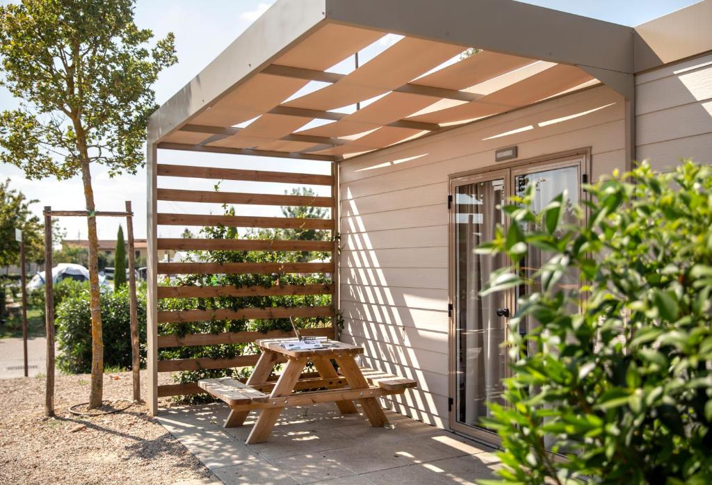 Wooden pergola over a small patio with a kids picnic table and bench next to sliding glass doors, casting striped shade.