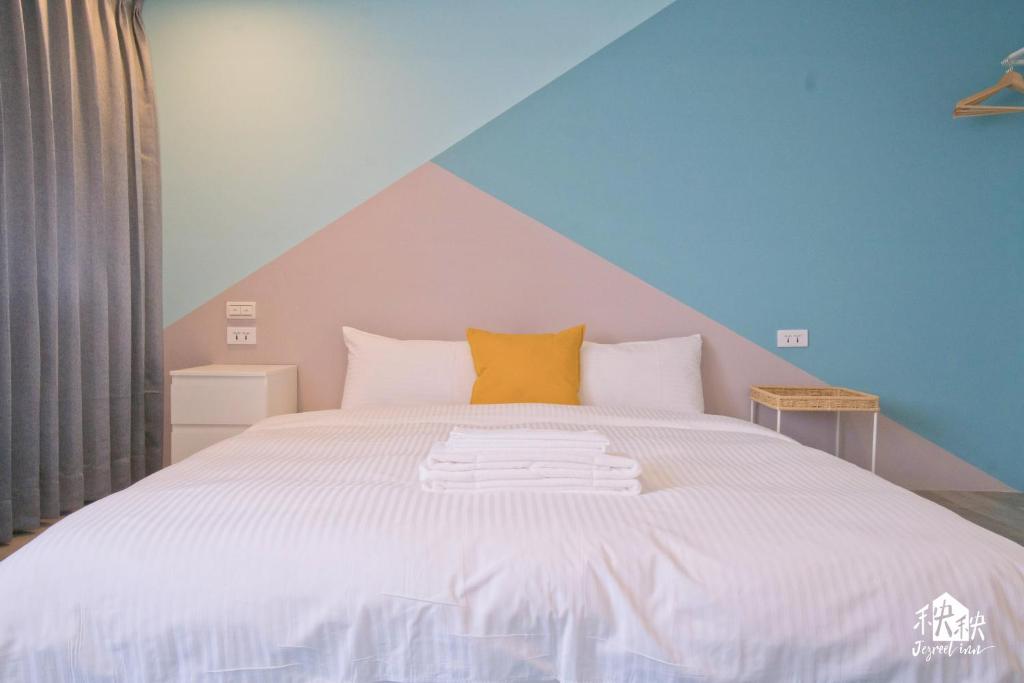 A neatly made bed against a pastel diagonal-wall mural, with a yellow accent pillow and folded towels on top.