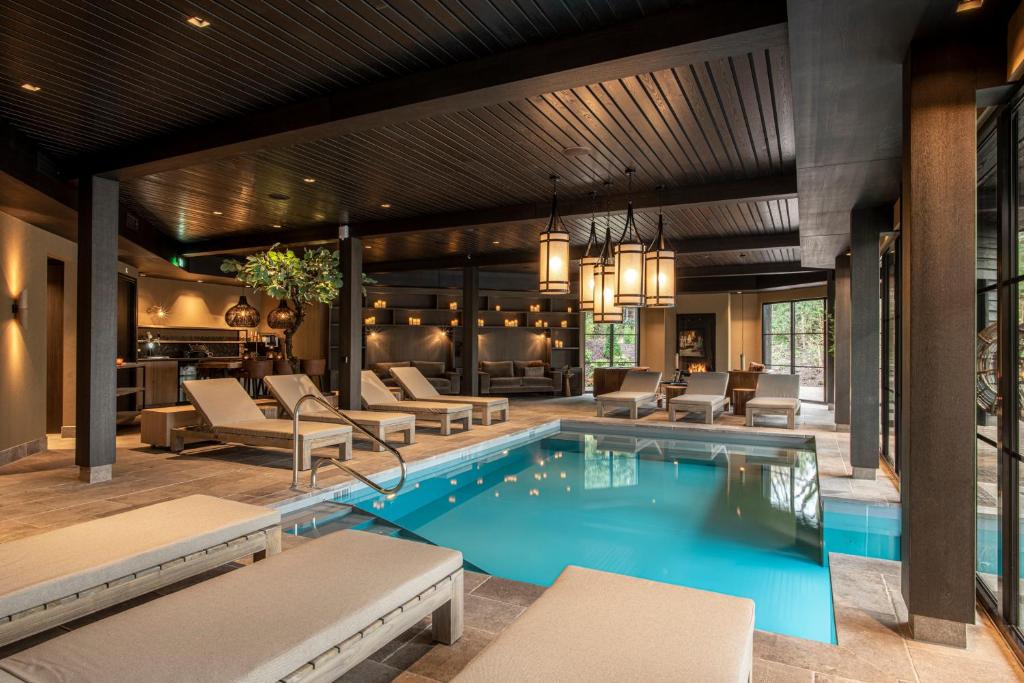Indoor hotel pool area with a rectangular turquoise pool, beige loungers lined along the edges, and a dark wood ceiling with hanging lanterns.
