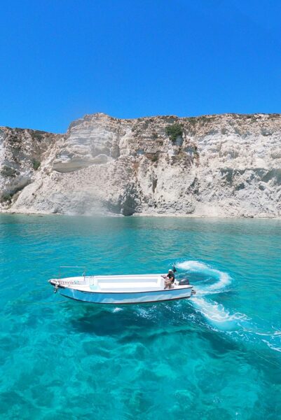 White motorboat gliding on clear turquoise water with white cliffs and a blue sky behind it, near the coast.