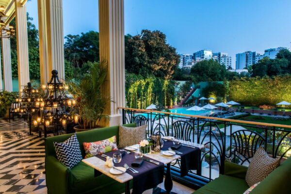 Luxurious outdoor restaurant terrace at dusk with green cushioned seating, a chandelier, and a pool view.