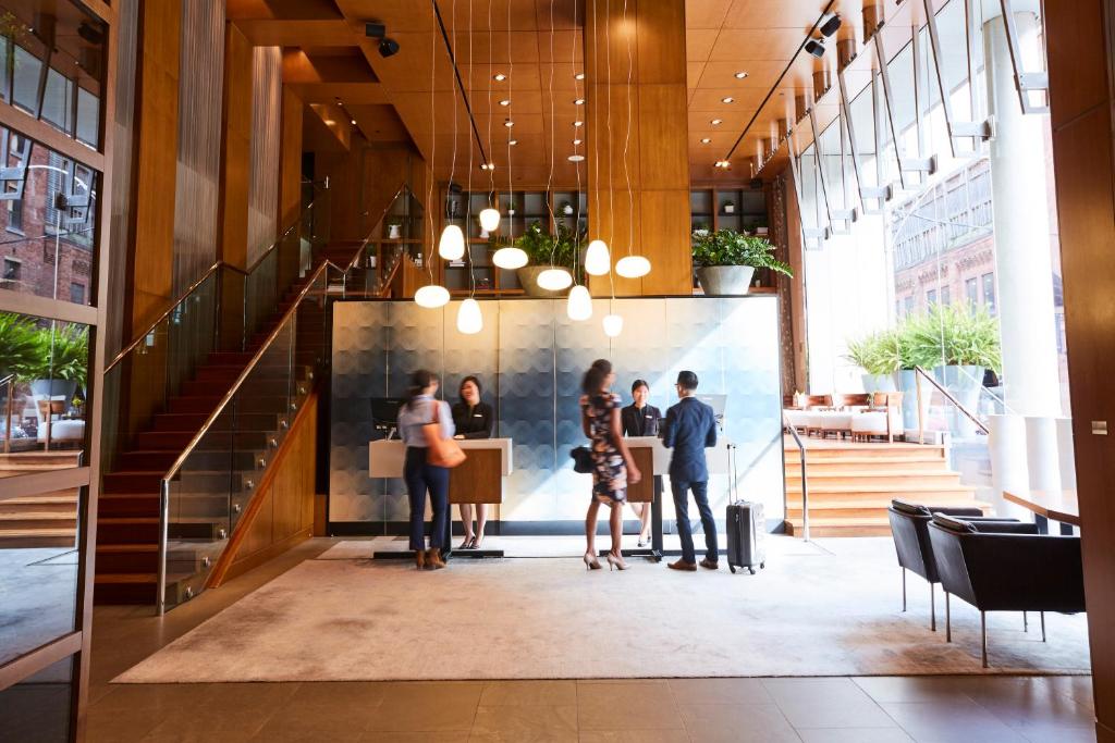 Reception desk in a modern hotel lobby with guests checking in and warm wood paneling around.