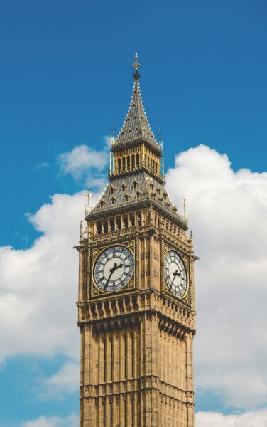 Elizabeth Tower (Big Ben) with ornate clock faces against a blue sky and clouds elsewhere in the frame, showing Gothic detailing.