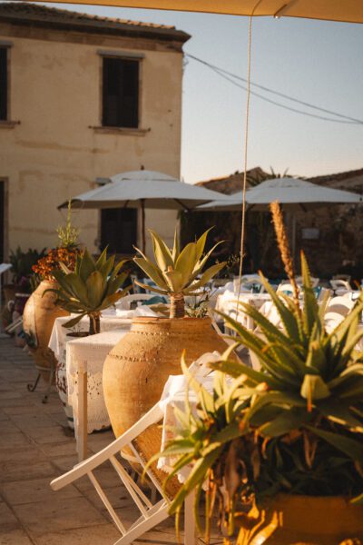 Outdoor dining area with large clay pots and agave plants on lace-draped tables under umbrellas.