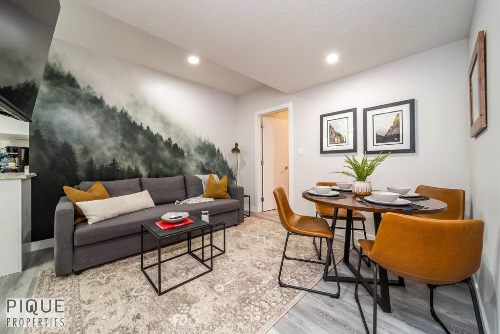 Living room and dining area: gray sofa with mustard pillows in front of a forest mural, black coffee tables, and a round dining table with four orange-brown chairs.