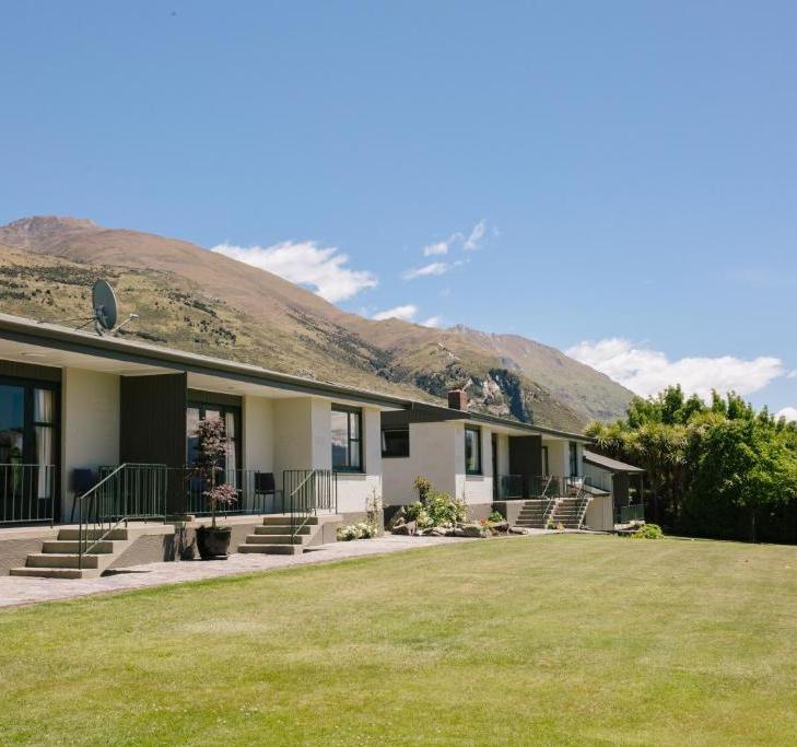 Row of single-story white houses with steps and small porches, a green lawn in front, and mountains under a blue sky in the background.
