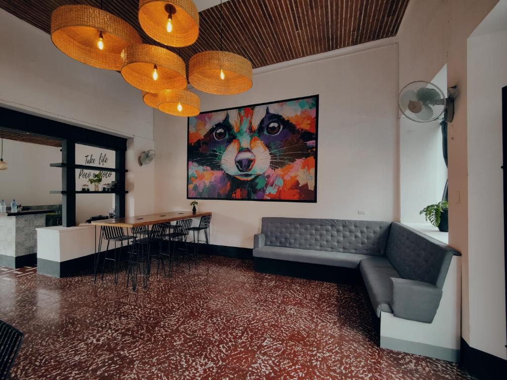 Cafe seating area with a row of high wooden tables and metal chairs under warm woven pendant lights, a colorful fox painting on the wall, gray tufted sofa, and terrazzo floor.