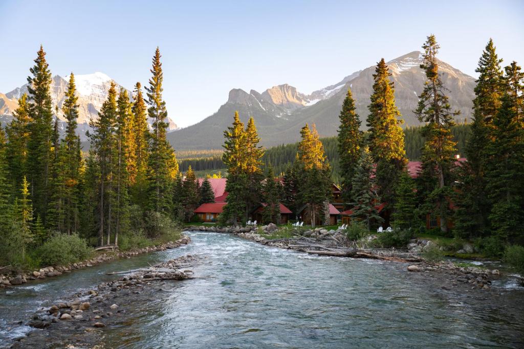 River runs through a forested valley with red-roof cabins and snow-capped mountains in the background.