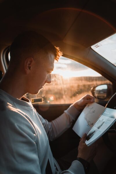 Man sitting in a car, reading a map or travel brochure as sunlight pours in through the window.