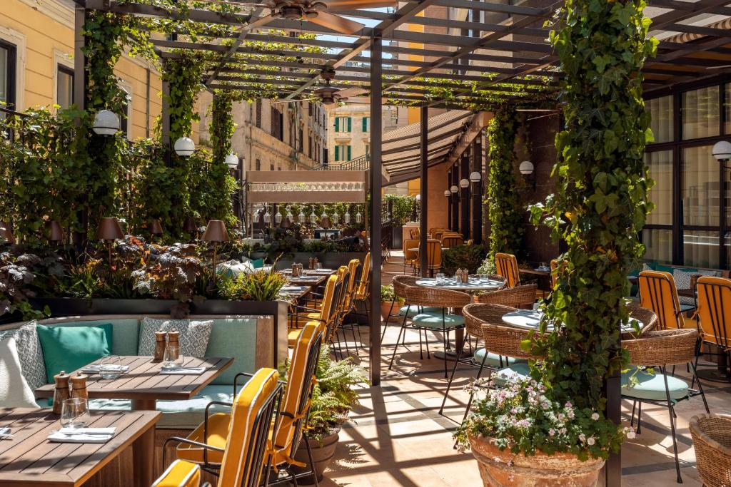 Sunny outdoor restaurant terrace with wooden tables, yellow chairs, wicker seating, and climbing vines under a pergola.