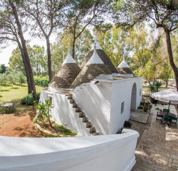 White cone-roofed trulli houses with stone stairs in a sunlit garden setting.