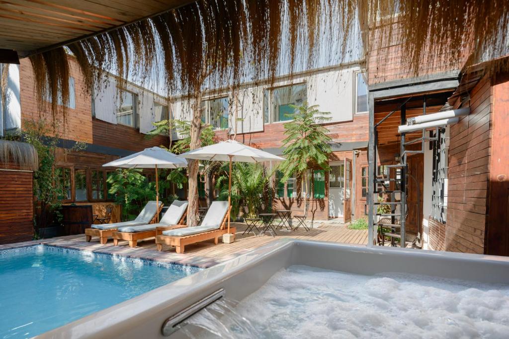 Poolside courtyard with wooden loungers, white umbrellas, and a bubbling hot tub in the foreground.