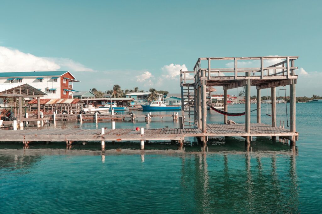 Coastal marina with wooden docks, small boats, and colorful waterfront houses under a clear blue sky.