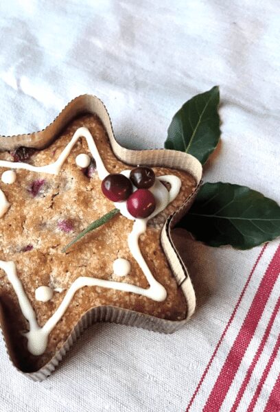 Star-shaped loaf cake with white icing zigzag, berries on top, placed on a striped cloth with green leaves nearby