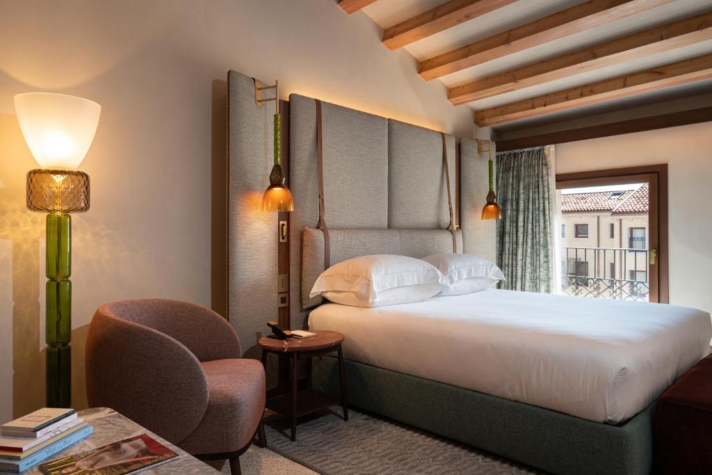 Hotel bedroom with a king bed, tall upholstered headboard, and pendant lights on both sides by a windowed balcony door.