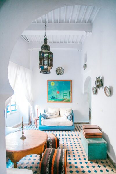 Bright coastal living room with a turquoise sofa, white cushions, and Moroccan lantern hanging from the ceiling; blue-and-white tiled floor.