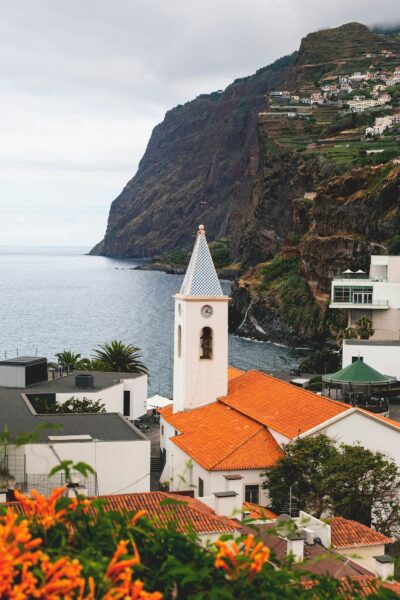 Coastal town perched on a cliff by the sea, with orange tiled roofs and a clock tower in the foreground.