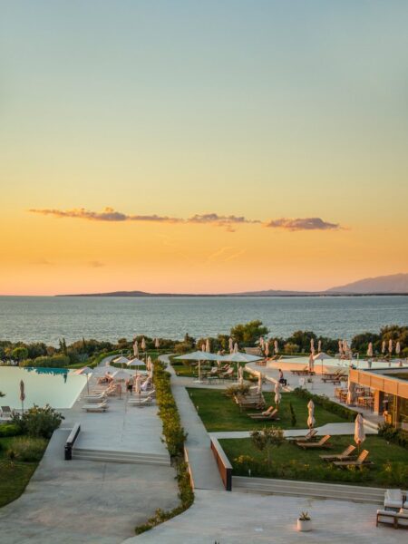 Resort pool area at sunset with lounge chairs, umbrellas, and manicured gardens overlooking the sea.
